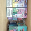 Schachtel mit bunten Verpackungen für E-Zigaretten oder E-Liquids mit “4 in 1” und Zeichentrickfiguren;, gestapelt in einem Karton mit Warnhinweisen auf der Vorderseite.