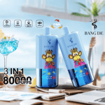 Deux appareils de vape BANG DE bleus avec un singe de dessin animé portant une couronne, posés sur une table avec un cocktail, des tranches de citron et un arrière-plan flou en bord de plage, mettant en évidence ' 3 EN 1 ', ' 80 000 PUFFS ' et les caractéristiques du produit.
