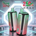 Dos dispositivos vapeadores desechables Bang King verdes y rosados con cuerpos degradados, pantallas digitales y boquillas verdes en un entorno metálico futurista.
