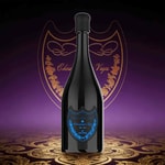 A tall, dark bottle with a rounded black cap, blue ornate label on the front, standing on a decorative purple-gold patterned surface with a heart-shaped emblem in the background.