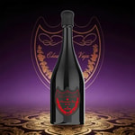 A tall dark bottle with a rounded black cork sits on a patterned golden and purple backdrop, featuring a red ornate shield label.