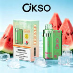 Dispositivo di vaporizzazione Okso Lush Ice verde brillante con confezione abbinata, incastonato tra fette di anguria e cubetti di ghiaccio su uno sfondo blu.