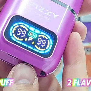 A close-up of a purple Fizzy vape device with a glowing blue digital display, held between fingers; text in the corner reads “50000 PUFF” and “2 FLAVORS IN 1.”