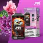 Un'immagine promozionale che mostra un dispositivo di vaporizzazione etichettato "JNR" con la grafica di un'aquila, accompagnato da uva e fiori di ciliegio sullo sfondo. Il dispositivo è mostrato insieme alla sua confezione, che evidenzia il sapore "Sakura Grape" e contiene un avvertimento sulla dipendenza dalla nicotina.