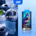 Gros plan de myrtilles sur glace avec une bouteille de produit bleu à saveur de framboise étiquetée " JNR Just No Reason Blue Razz Ice " avec une illustration colorée de faucon.