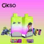Two OKSO double flavor disposable vape devices with green and pink gradient design, featuring red energy ice and grape ice flavors, an illustrated monkey with a hat, and energy drink and grape images on a gradient background.
