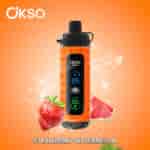 OKSO Shishai vape device with an orange design featuring digital display, surrounded by splashes of water, a strawberry, and watermelon slices, with the flavor 'Strawberry Watermelon' labeled below.