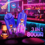 Two brightly colored BANG DE 3-in-1 disposable vape devices with cartoon monkey graphics are displayed in a neon-lit bar setting with bottles and glasses on the counter.