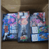 Several colorful packages of vaping products are arranged inside a cardboard box, featuring bold graphics and prominent warnings, indicating they are disposable devices with various puff counts.
