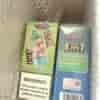 Two boxed vape products with bright colorful packaging, one green bottle design labeled “4in1” beside a blue box with listed flavors and a warning label.