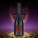 Une grande bouteille sombre avec un bouchon noir arrondi repose sur un fond à motifs dorés et violets, avec une étiquette de bouclier ornée de rouge.