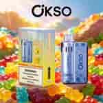 Gummy Bear flavored OKSO vape device with blue patterned pod and a matching box, set among colorful gummy candies outdoors.