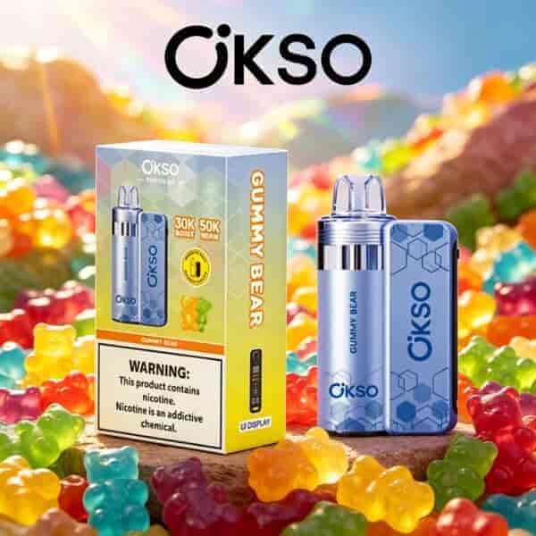 Gummy Bear flavored OKSO vape device with blue patterned pod and a matching box, set among colorful gummy candies outdoors.