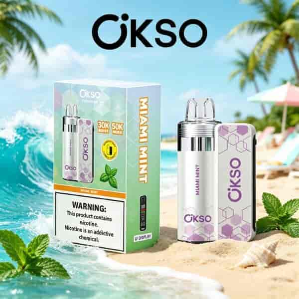 A boxed OKSO Miami Mint vape kit on a sandy beach with a minty bottle and a pastel purple patterned device, palm trees and blue ocean in the background.