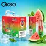 Scatole di prodotti Ökso Tornado rosso brillante con foglie di menta, fette di anguria e cubetti di ghiaccio su uno sfondo sfumato blu-verde.