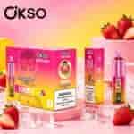 Sfondo sfumato rosa e giallo con scatole rosa etichettate OKSO Tornado, fragole e cubetti di ghiaccio sparsi su una superficie rosa.